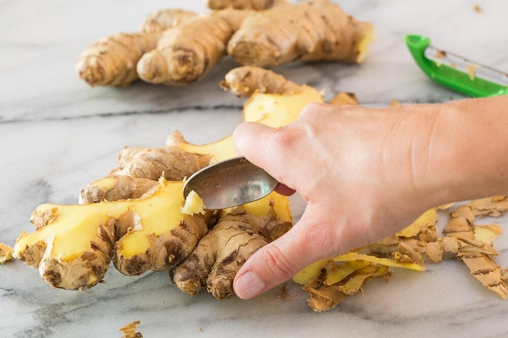 Чистка имбирного корня ложкой Девушка чистит корень имбиря