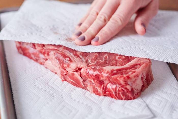 Промытое и обсушенное мясо Девушка обсушивает мясо салфетками