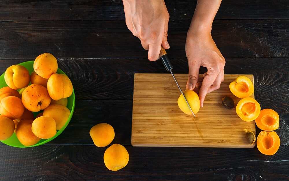 Подготовка свежих плодов к сушке Девушка режет абрикосы и удаляет косточки