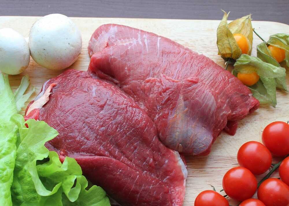 Подготовка свежего мяса к вялению Два куска свежего мяса на деревянной доске