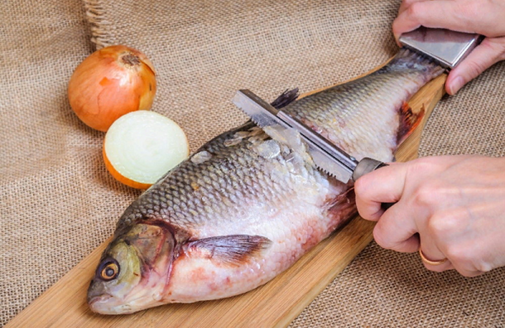 Повар очищает леща от чешуи Повар чистит рыбу