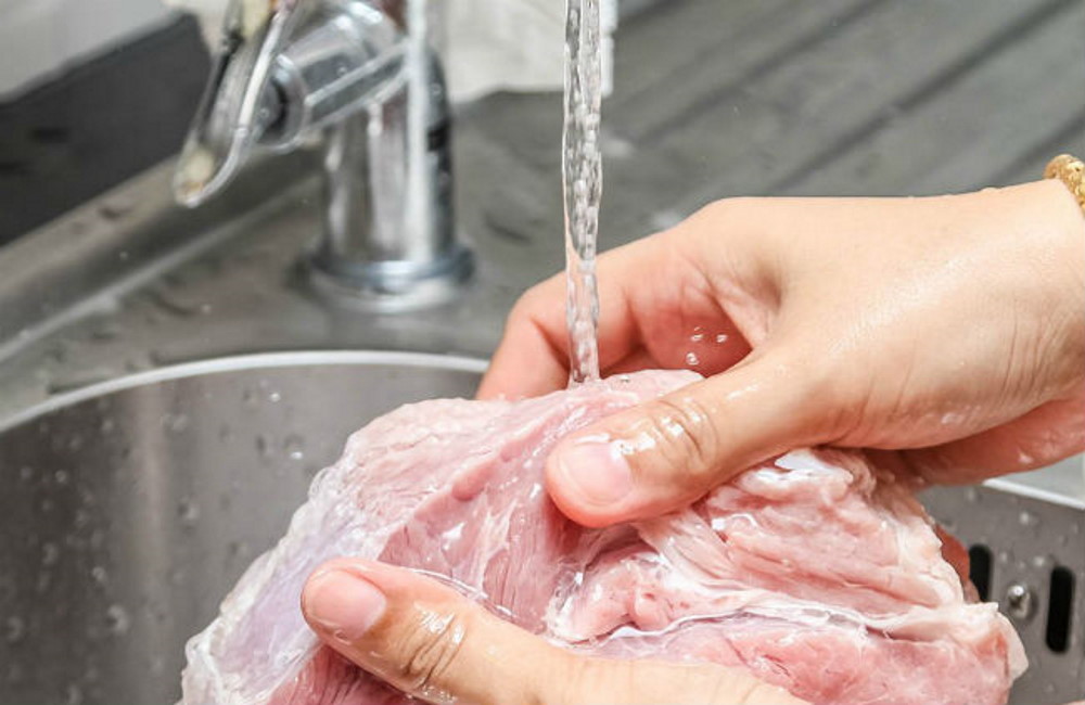 Повар промывает свежее мясо Повар промывает мясо под струёй воды