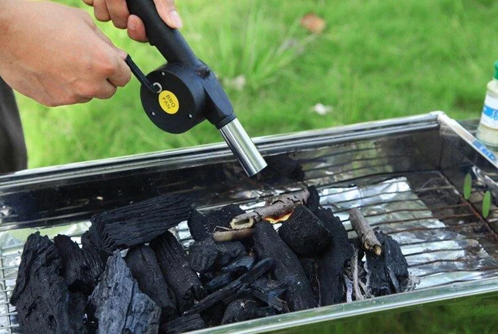 Мужчина использует ручной раздуватель для розжига Ручным раздувателем разжигают огонь