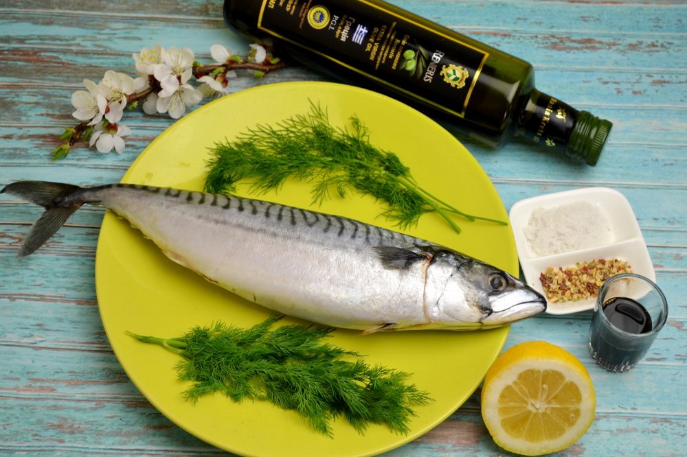 Скумбрия лежит на желтой тарелке, вокруг ингредиенты для маринада На желтой тарелке лежит свежая скумбрия с укропом, вокруг тарелки пряности, лимон, масло