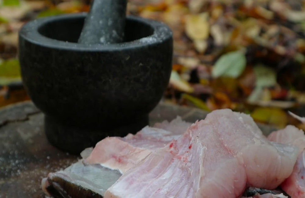 Свежий толстолобик и ступка со специями Ступка со специями рядом с рыбой