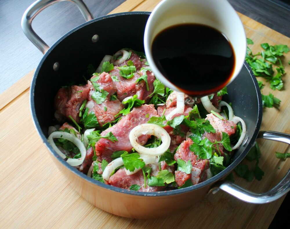 Куски свинины поливают соевым соусам Кастрюля с кусками свинины и лука поливают соевым соусом