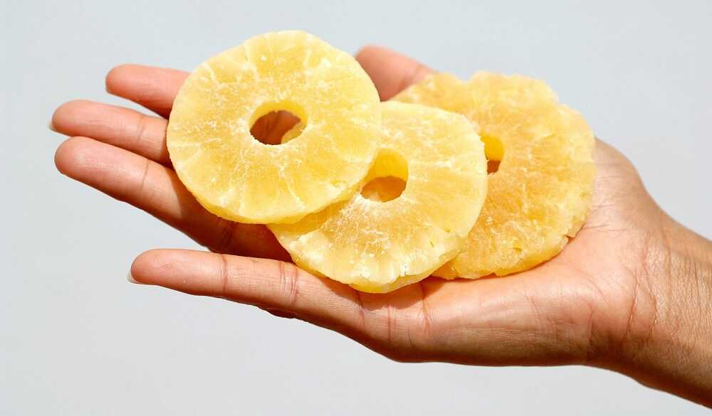 Дольки сушеного ананаса в руке Три кусочка сушеного ананаса лежат на ладони