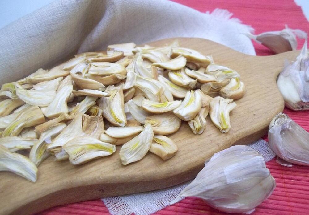 Сушеный кусочками чеснок Зубчики сушеного чеснока на разделочной доске
